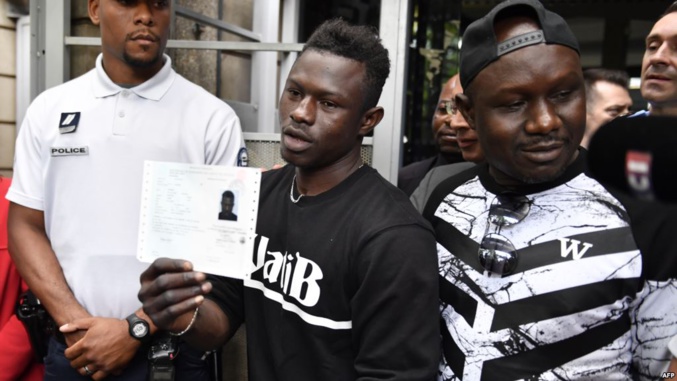 Le migrant malien Mamoudou Gassama avec son frère aîné, détient son permis de séjour temporaire après l'avoir reçu à la Préfecture de Bobigny, au nord-est de Paris, le 29 mai 2018.